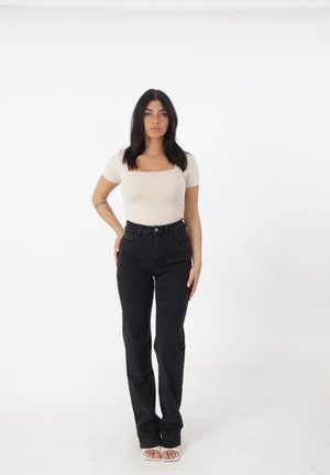 Jeans neri a vita alta con un design a gamba dritta, abbinati a un top aderente a maniche corte di colore crema. Tessuto liscio, hardware minimal.