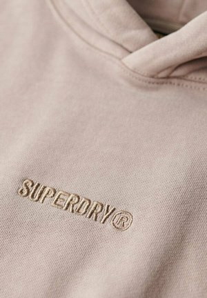 Lyserød hoodie lavet af blødt stof med et broderet "SUPERDRY®" logo i en matchende farve på brystområdet.