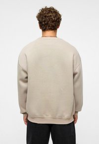 Beige sweatshirt met een relaxed fit, ribgebreide manchetten en zoom. Heeft een subtiel gewatteerd ontwerp op de achterkant. De stof lijkt zacht en casual.