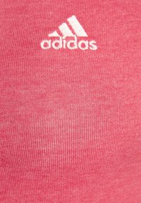 Tela de punto rosa con textura suave que presenta un logo blanco de Adidas y tres rayas en la esquina superior izquierda.