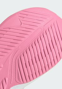 Suela de zapato con goma texturizada en un vibrante color rosa, con surcos verticales y horizontales que ofrecen agarre y durabilidad. Se aprecian acentos laterales en blanco.