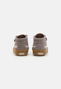 Sive nubuck visoke tenisice s bijelim bočnim prugama i smešnim gumenim đonom. Imaju podstavljeni ovratnik i Vans logo na peti i jeziku.