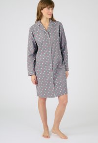 Pigiama da notte grigio con pois rosa e blu, maniche lunghe, colletto a scollo a V e chiusura con bottoni. Presenta piping bianco lungo i bordi.