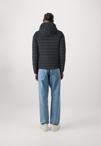 Zwarte pufferjas met een capuchon, horizontaal gestikt ontwerp, gecombineerd met lichtblauwe wijde jeans en witte sneakers. Eenvoudige, minimalistische look.