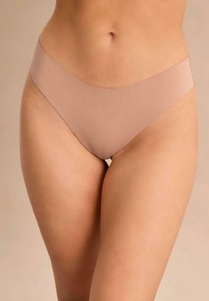 Kobieta w bezszwowej bieliźnie bikini w kolorze cielistym na neutralnym tle.