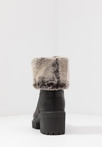 Črne usnjene gležnjarje z sivim umetnim krznom na zgornjem delu, ki imajo širok blokast peto in teksturiran podplat. Oznaka blagovne znamke vidna na peti.