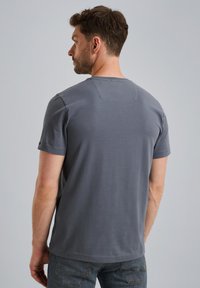 Siva majica s kratkimi rokavi in okroglim izrezom iz mehkega materiala, enostavnega dizajna, z manjšim našitkom na rami in ravnim robom.