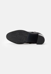 Semelle de chaussure noire présentant une surface en caoutchouc texturé avec un motif gaufré. Forme courbée avec un talon robuste pour la stabilité.