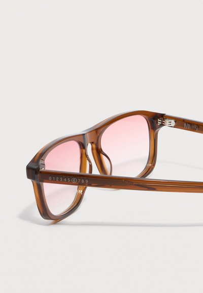 Καφέ διαφανή ορθογώνια γυαλιά οράσεως με ροζ απόχρωση στους φακούς και αριθμητικές λεπτομέρειες στο σκελετό, ακουμπισμένα σε λευκή επιφάνεια.