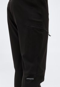 Lähivõte mustadest Patagonia pükstest, millel on lukuga reietasku ja nähtav brändilogo põlve kohal.