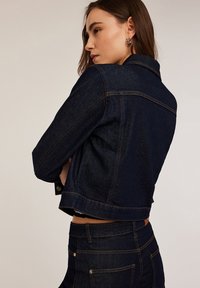 Donker denim cropjack met een getailleerd ontwerp, zichtbare oranje stiksel en klassieke kraag; gecombineerd met bijpassende denim broek.
