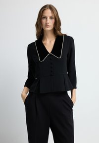 Černý peplum top s sametovým límcem, zdobený perlami podobným lemováním a předními knoflíky, doplněný o př tailored černé kalhoty.