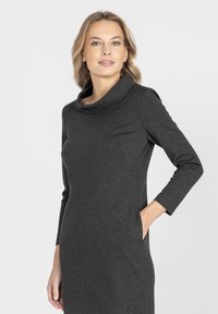 Sukienka w kolorze grafitowego węgla z kołnierzem typu komin, długimi rękawami i boczną kieszenią. Tkanina wydaje się gładka i elastyczna, o dopasowanym kroju.