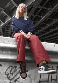 Navy sweatshirt with zip collar, oversized fit; red sweatpants; brown and black high-top sneakers with white accents; textured concrete background.