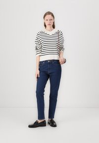Pull en maille rayé crème et marine ; jeans bleus ; mocassins noirs ; accessoires minimalistes ; fond uni.