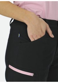 Svarta byxor med en rosa dragkedjeficka och en svensk flagga som accent. Har en slim fit och en mjuk textur. Närbild av fickområdet.
