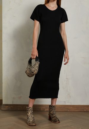 Kobieta ubrana w czarną sukienkę midi z krótkim rękawem, trzymająca torebkę w zebrowy wzór i nosząca pasujące botki w zebra.