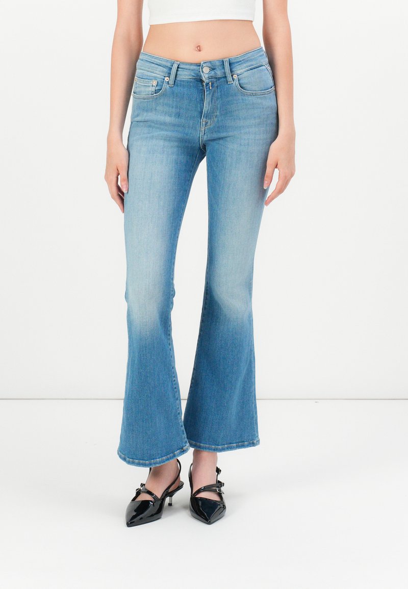 Hellblaue ausgestellte Jeans aus Denim mit hoher Taille und einem subtilen Verblassen, kombiniert mit schwarzen Lacklederschuhen.