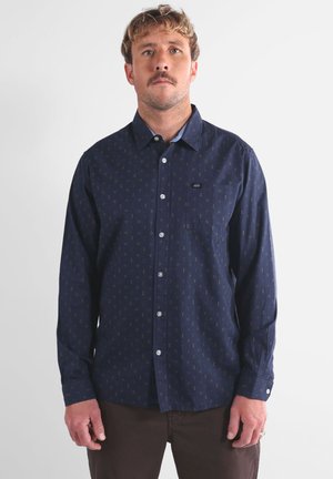 Chemise à manches longues marine avec un design à boutons, présentant un motif géométrique subtil, une poche unique et un col bleu clair contrastant.