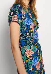 Bloemendress met korte mouwen, een blauw, groen, roze en gele bloemenpatroon op een donkere marineachtergrond, gemaakt van lichtgewicht stof.