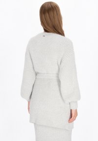 Lichtgrijze gebreide cardigan met een riem. Heeft een losse pasvorm, wijde mouwen en een ribbelstructuur. Geen zichtbare hardware of patronen.