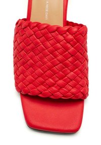 Sandale rouge à semelle plate avec une tige tressée, une texture lisse et une forme de bout carré pour plus de confort.