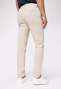 Beige chinos with a regular fit, featuring a back pocket and elastic waistband, paired with white sneakers on a neutral background.
