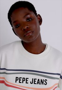 Sudadera blanca con rayas multicolores y el texto "PEPE JEANS" en negro. El cuello acanalado y la tela texturizada añaden detalles.