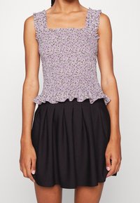 Fialový květinový top se smockovaným pasem a volánkovými ramínky, doplněný černou plisovanou sukní. Materiál je lehký s texturovaným povrchem.