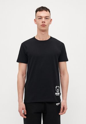 T-shirt nera in cotone, con scollo rotondo e maniche corte. Presenta una grafica di un orso bianco e il testo "MOSCHINO" vicino all'orlo.