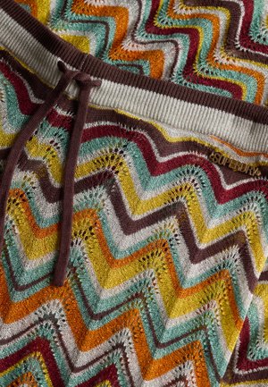 Tissu tricoté multicolore présentant un motif en zigzag en orange, jaune, turquoise, marron et blanc. Texture douce avec une taille côtelée et un cordon de serrage.