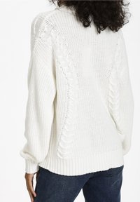 Biały, dziany sweter z wzorem w warkocze na ramionach i rękawach, z prążkowanymi mankietami i dołem oraz luźnym krojem.