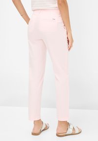 Rosa, figurbetonte Hose mit zwei Gesäßtaschen und einer glatten Textur. Getragen mit beigen Sandalen, die über einen Riemen und eine Schnallendetail verfügen.