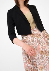 Svart cropped blazär med skräddarsydda axlar och en knapp, i kombination med en blommönstrad, ljus kjol med intrikata mönster.