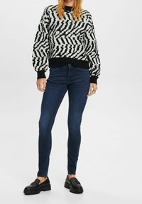 Jersey con estampado en blanco y negro, cuello redondo y mangas abullonadas, combinado con vaqueros ajustados azul oscuro y mocasines negros.