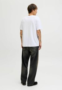 Camiseta blanca de algodón con un corte relajado, combinada con jeans de mezclilla gris oscuro con un acabado desgastado y bolsillos traseros visibles.