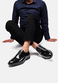 Zapatos de vestir de charol negro con punta redondeada, diseño de cordones y un acabado liso y brillante. Suela plana con adornos mínimos.