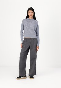 Light grey knitted sweater with a textured pattern, paired with loose dark grey cargo pants and black sneakers with white stripes.