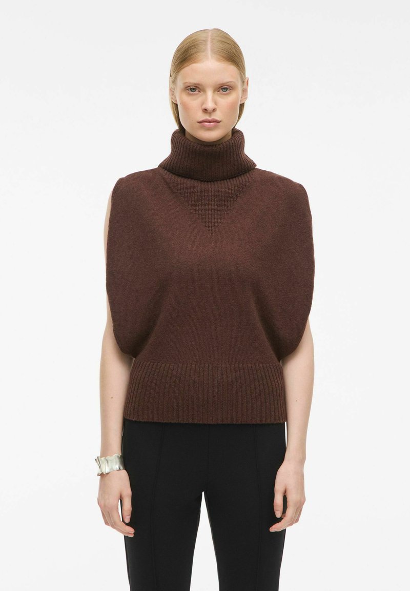 Tumša brūna īsām piedurknēm turtlenecka džemperis, ar ribotiem malām un tekstūrētām plecu detaļām. Pievienots sudraba rokassprādze.