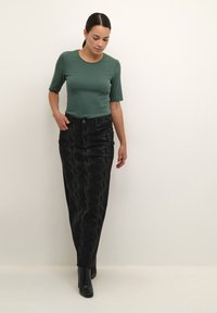 Un haut vert ajusté à manches courtes, associé à une jupe noire taille haute avec un motif texturé. Des bottines noires à la cheville complètent la tenue.