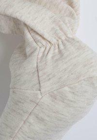 Tissu tricoté couleur crème avec un motif texturé, comportant des coutures froncées et des formes triangulaires. Matériau doux et léger.