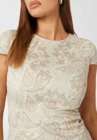 Šviesiai žalia suknelė su paisley raštu ir gėlių motyvais, apvaliu iškirpimu ir trumpomis rankovėmis, pagaminta iš lygaus audinio.