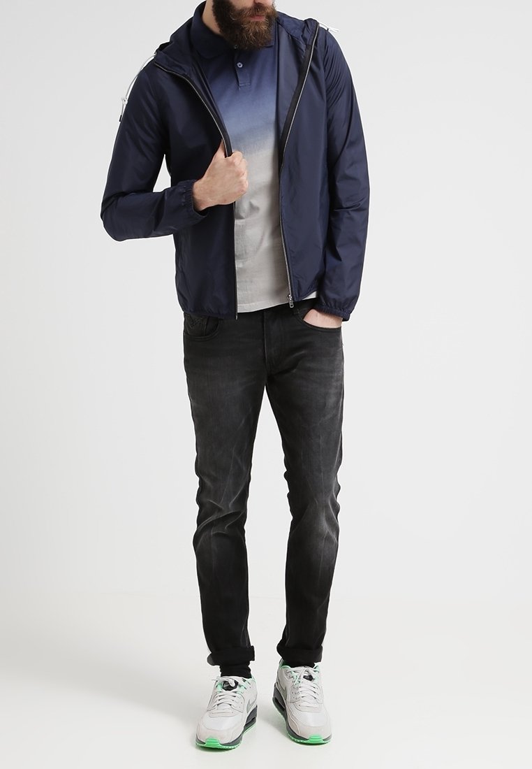 Marinblå huva-jacka, grå gradient polo, mörka jeans och grå sneakers med gröna accenter. Texturerad tyg, elastiska ärmslut och dragkedjestängning.