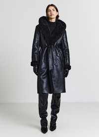 Cappotto in pelle nera con un colletto e polsini in velluto morbido e testurizzato. Presenta una chiusura a vita con lacci e un design dritto. Finitura lucida.