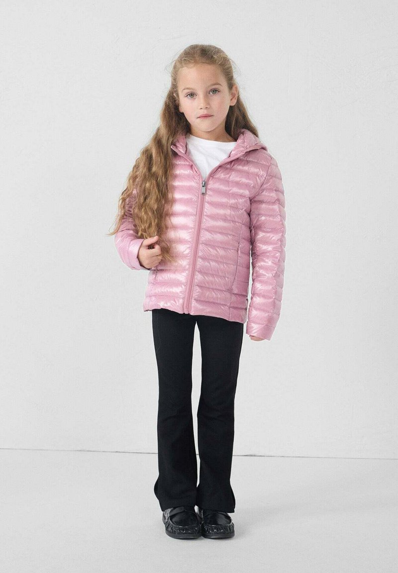 Giacca imbottita rosa con zip frontale, leggera, design trapuntato. Abbinata a pantaloni neri a zampa d'elefante e scarpe nere, con una camicia bianca sotto.