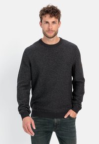 Dunkelgrauer Strickpullover mit Rundhalsausschnitt, gerippten Bündchen und Saum, der ein dezentes Strukturmuster aufweist. Über einer Jeans getragen.