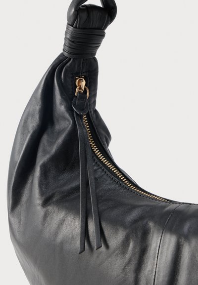 Sac à main en cuir noir avec une poignée nouée et une fermeture éclair dorée visible dotée de deux languettes en cuir.