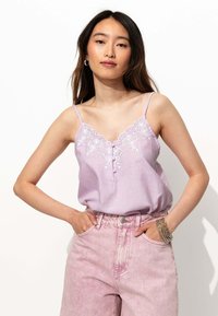 Débardeur lavande à rayures avec des accents brodés blancs, bretelles spaghetti réglables et un détail de bouton en bas, associé à un pantalon en denim rose.