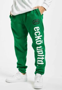Grønne træningsbukser lavet af blødt stof med en tapered design. Har "eckō unlt'd" trykt i hvidt og et logo på venstre lår.