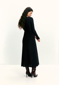 Hosszú ujjú fekete ruha, sima anyagból, testhezálló felsőrésszel és légies szoknyával. Pirosas-bordó hegyes orrú magassarkú csizmával párosítva.